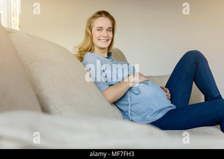 Portrait of smiling pregnant woman sitting on sofa at home Banque D'Images