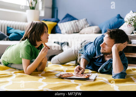 Père et fils de manger la pizza sur le plancher à la maison Banque D'Images