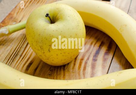 Deux bananes et yellow apple au milieu sur la surface en bois close up Banque D'Images