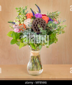 Un beau bouquet de fleurs, roses multicolores avec des feuilles vertes se trouve dans un vase en verre avec de l'eau sur une table marron clair Banque D'Images