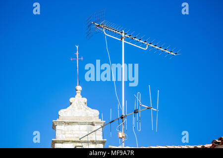 Deux vieux rusty blanc television antennas sur toit avec ciel bleu clair et flou avec l'église croix métallique sur le dessus en Grèce Banque D'Images