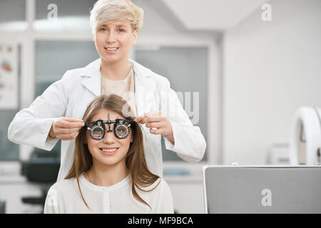 Façade de young smiling girl est assis et à la caméra à vision au cours de la vérification. Ophtalmologiste est, à l'aide de l'équipement médical pour sauver et d'améliorer la santé de l'œil. Banque D'Images