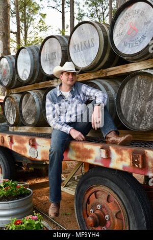 Western cowboy assis sur la remorque à plat avec des fûts de whisky ou de barils de Das Haus Peach, Fredericksburg, au Texas, USA. Banque D'Images