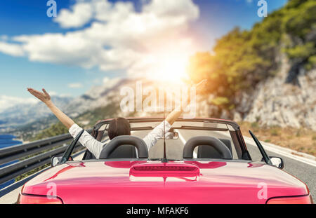 Jeune femme dans une voiture avec une décapotable sur la route de la mer sur fond de belles montagnes sur une journée ensoleillée. Une femme lève les bras vers le haut. Banque D'Images