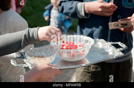 Main de l'enfant d'abord à obtenir des bonbons dans un bol en verre sur le plateau métallique tenue par femme, service des gens lors d'une cérémonie de Pâques, des activités de plein air Banque D'Images