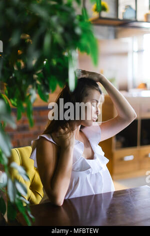 Fille avec main levée assis à table à côté de prix usine. Banque D'Images