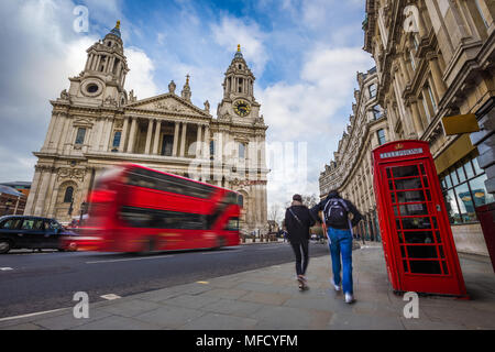 Londres, Angleterre - couple de touristes passent à côté d'un téléphone rouge traditionnel fort avec red bus double étage en déplacement à fond à St.Paul's Cathedra Banque D'Images