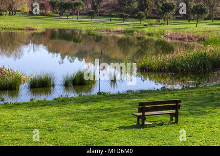 Banc de jardin donnant sur le lac/étang de Parque da Devesa parc urbain à Vila Nova de Famalicão, Portugal. Voir l'herbe verte des pelouses, et le lac. Banque D'Images