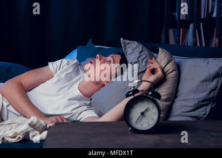 Portrait de brunet à l'insomnie au lit avec réveil Banque D'Images