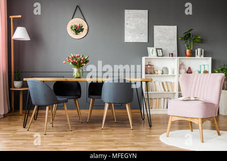 Fauteuil rose à côté de gray chaises table en bois avec tulipes en élégante salle à manger de l'intérieur Banque D'Images