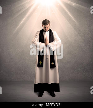 Un jeune prêtre religieux masculins en noir et blanc robe donnant sa bénédiction, tenant la sainte bible tout en étant éclairée par des rayons lumineux venant de concept ci-dessus Banque D'Images