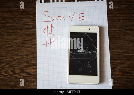 Smartphone avec un écran cassé sur une feuille de papier avec l'inscription de dollars. L'enregistrement Banque D'Images