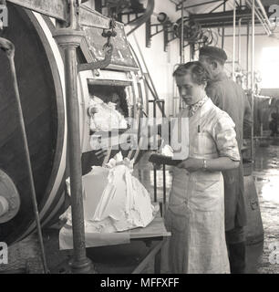 Années 1950, photo historique montrant une jeune femme dans une crémerie beurre Préparation à la main à l'aide de spatules en bois produit par un corps mécanique ou de désabonnement. La baratte a fait le beurre à partir de crème. Banque D'Images
