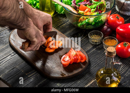 Chef de cuisine de l'homme dans la cuisine. La main de l'homme coupe carotte sur une planche en bois Banque D'Images