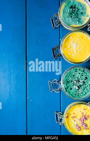 Gâteau au fromage sur un bocal en verre, faites à la mangue et de la spiruline en poudre, avec des graines de chia et de noix de coco en poudre, sur un fond bleu en bois Banque D'Images