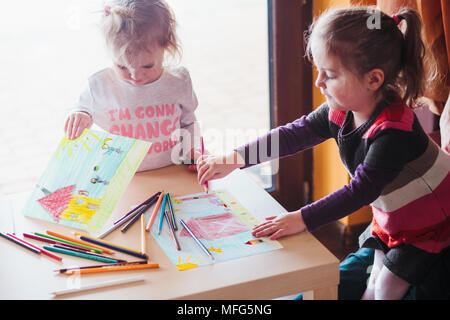 Deux petites filles dessiner une maison et des photos d'enfants qui jouent à l'aide de crayons de couleur à l'intérieur table debout Banque D'Images