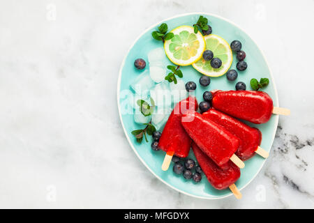 Jus de fraises congelées snack pop ou de glace sur un popsicle table en marbre blanc avec des bleuets et de la glace à la menthe. été la crème glacée fond d'aliments frais Banque D'Images