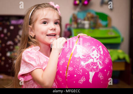 Petite fille dans une belle robe rose avec une balle dans la chambre des enfants Banque D'Images