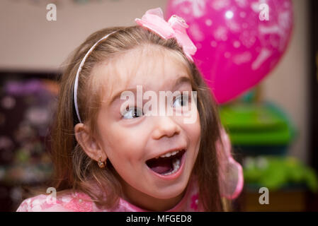 Petite fille dans une belle robe rose avec une balle dans la chambre des enfants Banque D'Images