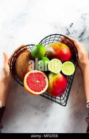 Les mains tiennent un panier sous la forme d'un coeur avec des fruits exotiques . Photo de dessus. copier l'espace. sur une table de marbre blanc Banque D'Images
