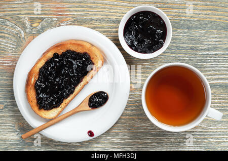 Tasse de thé et de délicieux toasts avec de la confiture de bleuets pour le petit-déjeuner sur la vieille table en bois, vue du dessus Banque D'Images