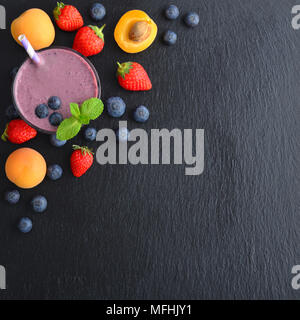 Verre de smoothie shake aux fruits ou avec des pailles à boire et des fruits et baies sur fond ardoise, vue du dessus Banque D'Images