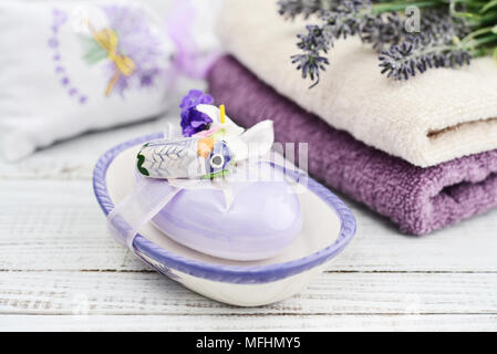 Savon lavande avec un décor en forme de papillons de nuit dans une boîte de savon avec un bouquet de lavande et de serviettes sur un fond de bois Banque D'Images