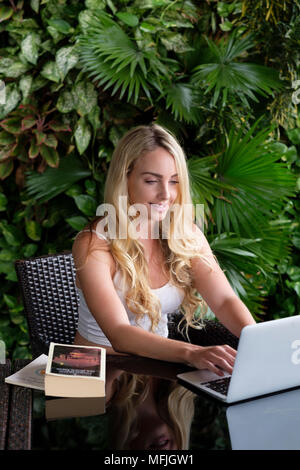 Young Caucasian woman backpacker portant un gilet blanc haut et assis à une table en Asie travailler sur un ordinateur portable, le Vietnam, l'Indochine, l'Asie du Sud-Est, Asie Banque D'Images