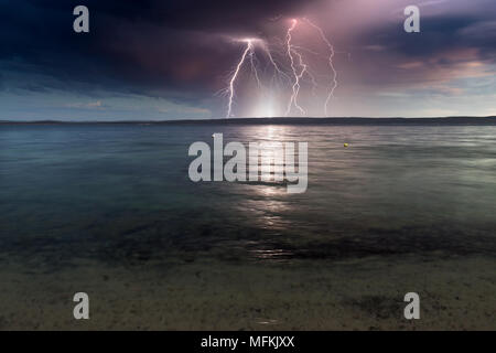 Des éclairs spectaculaires sur une baie de l'océan calme sur un inquiétant, sombre, contrastant jour de tempête. Banque D'Images