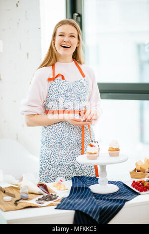 Demi-taille portrait d'une belle femme décorant des cupcakes et souriant. Beaux cupcakes chef cuisinier à la maison Banque D'Images