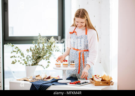 Belle femme heureuse sourire agréablement la décoration de cupcakes avec berry sur la table de chambre bien éclairée Banque D'Images