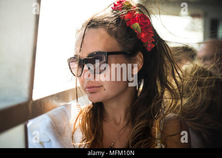 Jeune femme avec des roses en coiffure et rayons de soleil sur son visage. Jolie fille à la recherche d'une fenêtre. Vue rapprochée. Banque D'Images