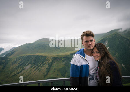 Jeune couple s'établit à plate-forme d'observation sur fond de belles montagnes vertes. Happy woman with long hair embrasse avec bel homme. Banque D'Images