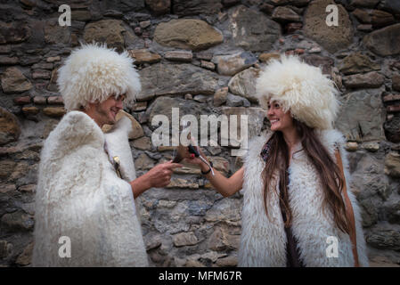 Drôle de couple dans les vêtements en laine sont de boire des verres traditionnels. Smiling man avec de jeunes femme boit à la santé sur fond de pierre. Banque D'Images