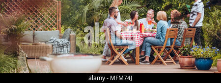 Groupe d'amis de manger des grillades au cours de séance dans la cour Banque D'Images