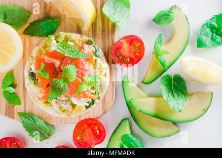 Pain croustillant collation santé avec du saumon, du fromage cottage, purée d'avocat, des tomates cerises, menthe, jus de citron, poivre. Petit-déjeuner facile gros plan sur un w Banque D'Images