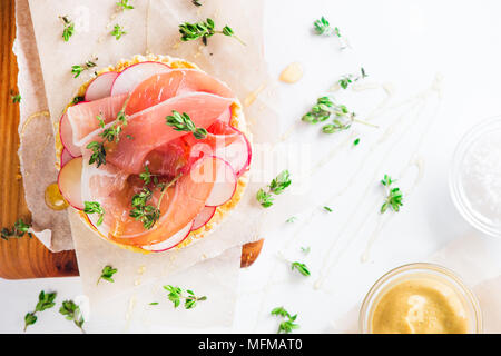 Pain croustillant collation santé avec jambon de Parme, tranches de radis, moutarde, sel de mer, miel et thym frais. Petit-déjeuner facile gros plan sur un fond blanc avec Banque D'Images