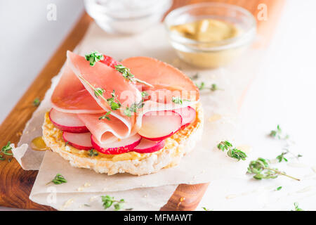 Pain croustillant collation santé avec jambon de Parme, tranches de radis, moutarde, sel de mer, miel et thym frais. Petit-déjeuner facile gros plan sur un fond blanc avec Banque D'Images