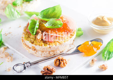 Pain croustillant collation santé avec jambon de Parme, noix, moutarde, confiture d'abricot, de feuilles de basilic frais. Petit-déjeuner facile gros plan sur un fond blanc avec copie s Banque D'Images