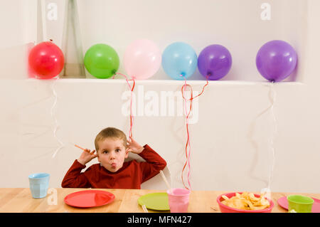 Portrait d'un garçon assis à une table et de faire un visage Ref : crédit obligatoire : Banque D'Images