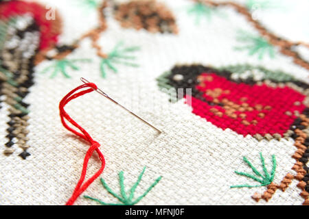 Broderie au point de croix avec aiguille et fil rouge. Bouvreuil rouge sur un sapin macro broderie close up. Vue de dessus. Banque D'Images