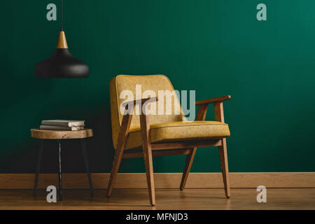 Vintage jaune, fauteuil, petite table avec des livres et lampe noire situé sur l'intérieur du mur dans la salle de séjour Banque D'Images