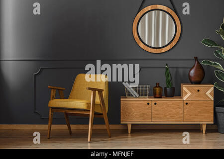 Salon intérieur avec miroir rond, armoire en bois et un fauteuil rétro situé sur la moulure de mur gris avec Banque D'Images