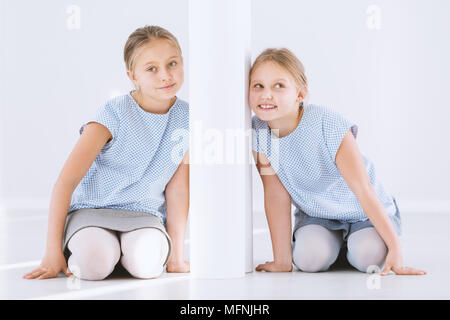 Portrait de jeunes, professionnels des soeurs jumelles à genoux et appuyé contre d'autre d'un mur blanc Banque D'Images