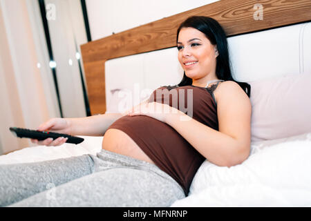 Beautiful pregnant woman watching TV Banque D'Images