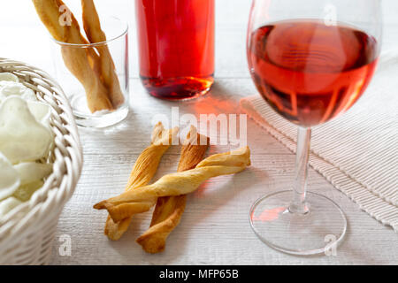 Verre de vin rose avec des collations et du vin parti Bouteille sur table en bois blanc rustique. Banque D'Images