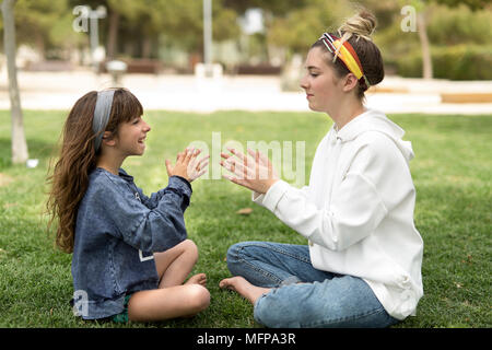 Deux soeurs jouant dans un parc assis sur l'herbe. Pris dans un parc dans la ville de San Vicente del Raspeig dans la province d'Alicante en Espagne. Banque D'Images