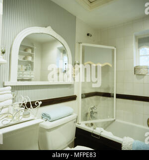 Une salle de bain traditionnelle contenant du papier peint à rayures bleu et blanc carreaux avec un grand miroir semi-circulaire au-dessus des toilettes. Banque D'Images