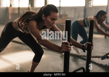 Jeune femme forte poussant le prowler équipement d'exercice. La femme de l'exercice à la salle de sport. Banque D'Images