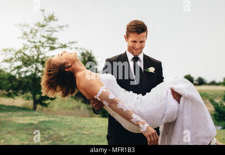 Groom Smiling bride comptable sur les armes au parc. Beautiful wedding couple avec groom soulevant sa mariée et la marche à pied. Banque D'Images